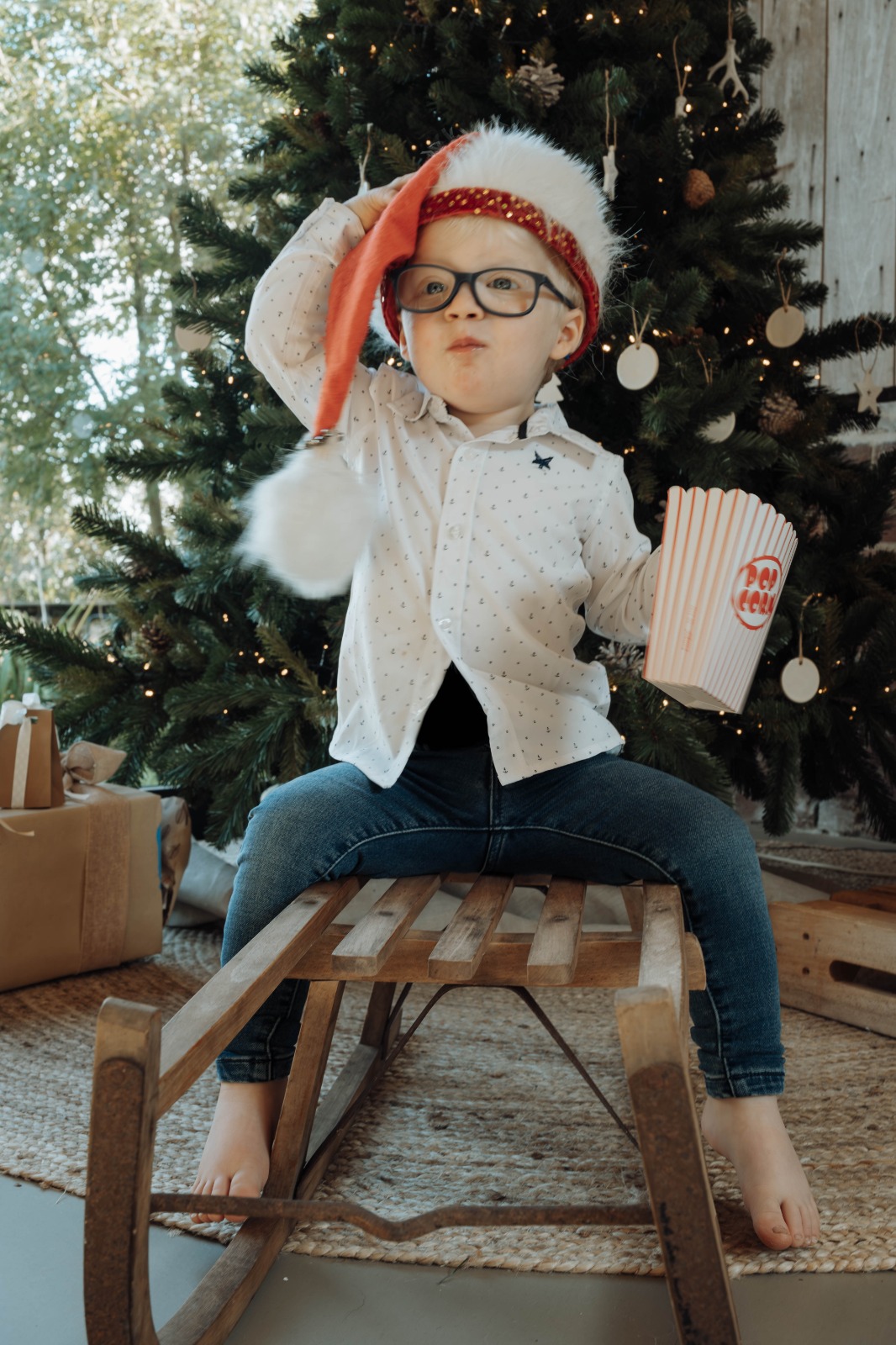 Jongen met kerstmuts en popcorn bij de kerstboom