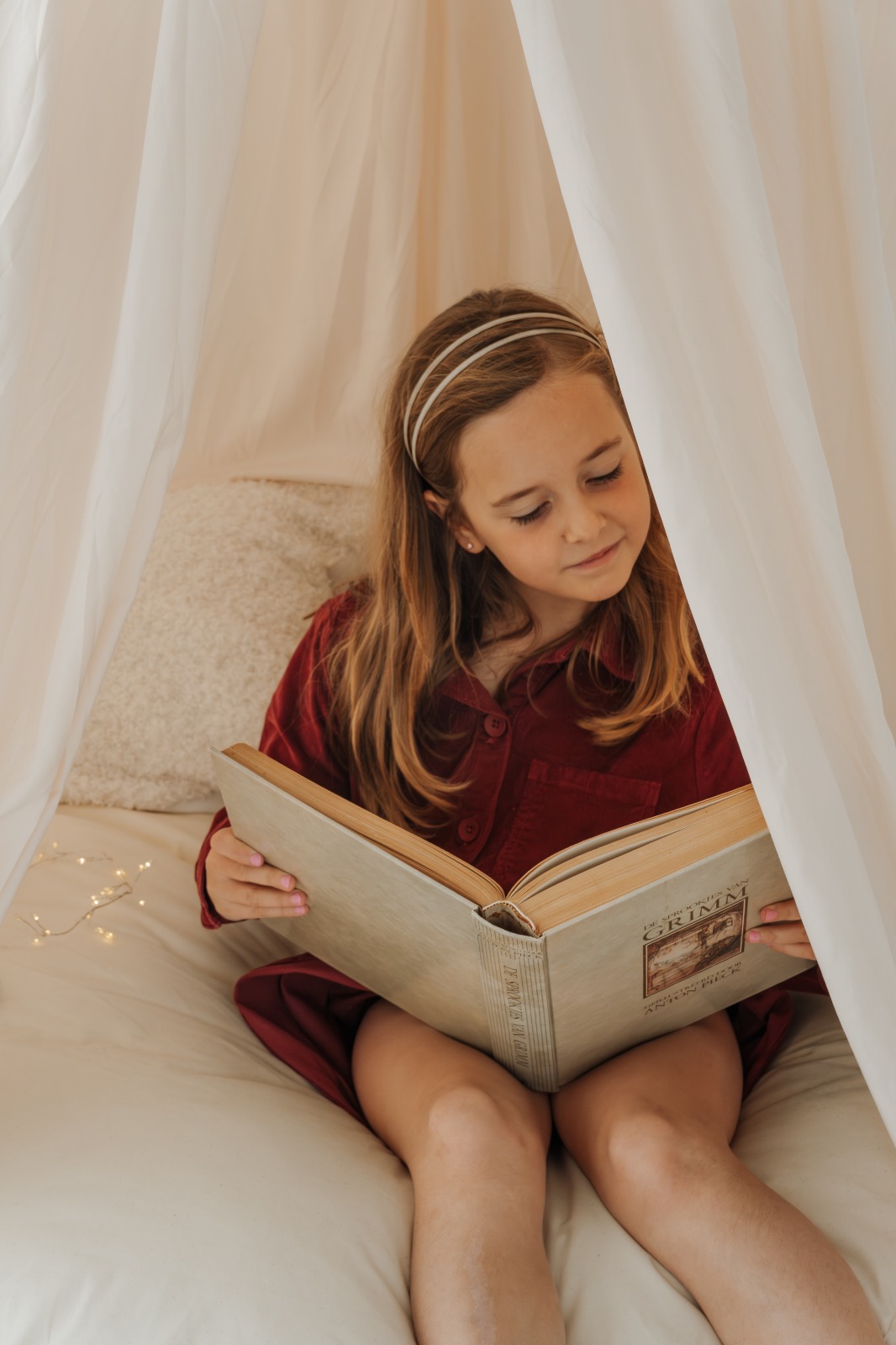 Meisje leest een boek in een bedtentje met lichtjes